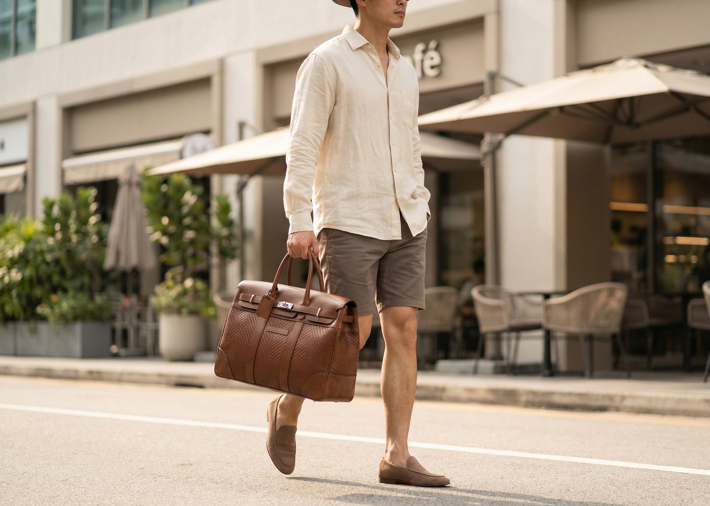 Man in linen shirt carrying a brown leather Brunello Cucinelli Travel Bag with woven details from The Exclusive Line Singapore.